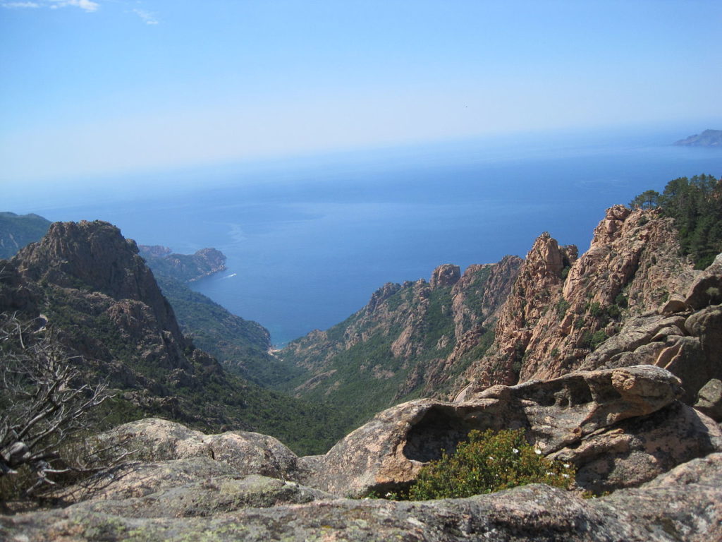 Una vista desde lo alto de la cordillera de Córcega hacia el mar azul con montañas rocosas y poca vegetación