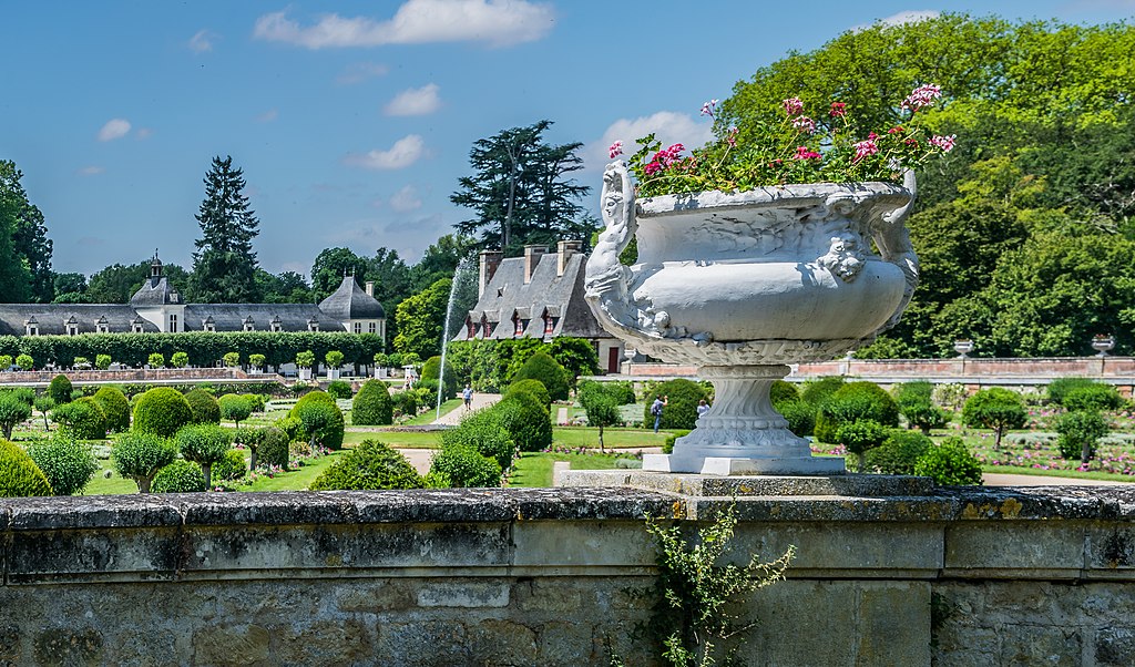 Jardín de Diane de Poitiers en Chenonceau Chateau en el Valle del Loira. Mirando por encima de un antiguo muro de piedra y una enorme urna de piedra llena de flores en una hilera de macizos de flores formales con edificios bajos en el fondo