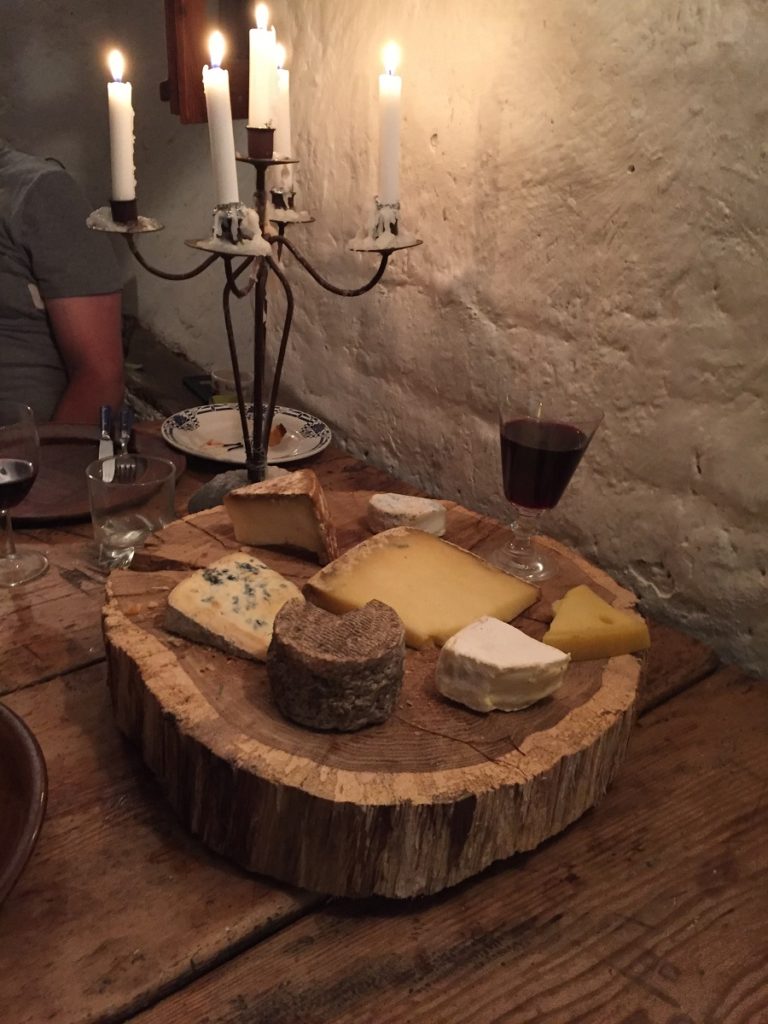 quesos en un bloque de madera con una copa de vino y un candelabro detrás contra una pared rústica blanca