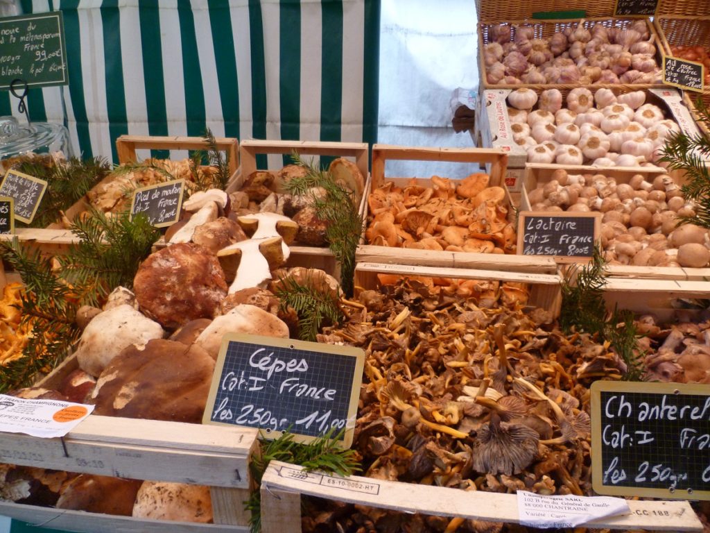 varios champiñones en caja con precios en pizarras en un mercado francés