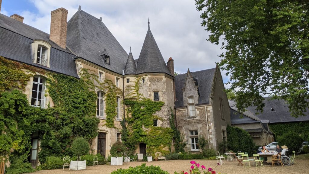 Castillo de Bazouges Clós Glenloir con figuras en un lado y edificios del castillo con techos y torres detrás