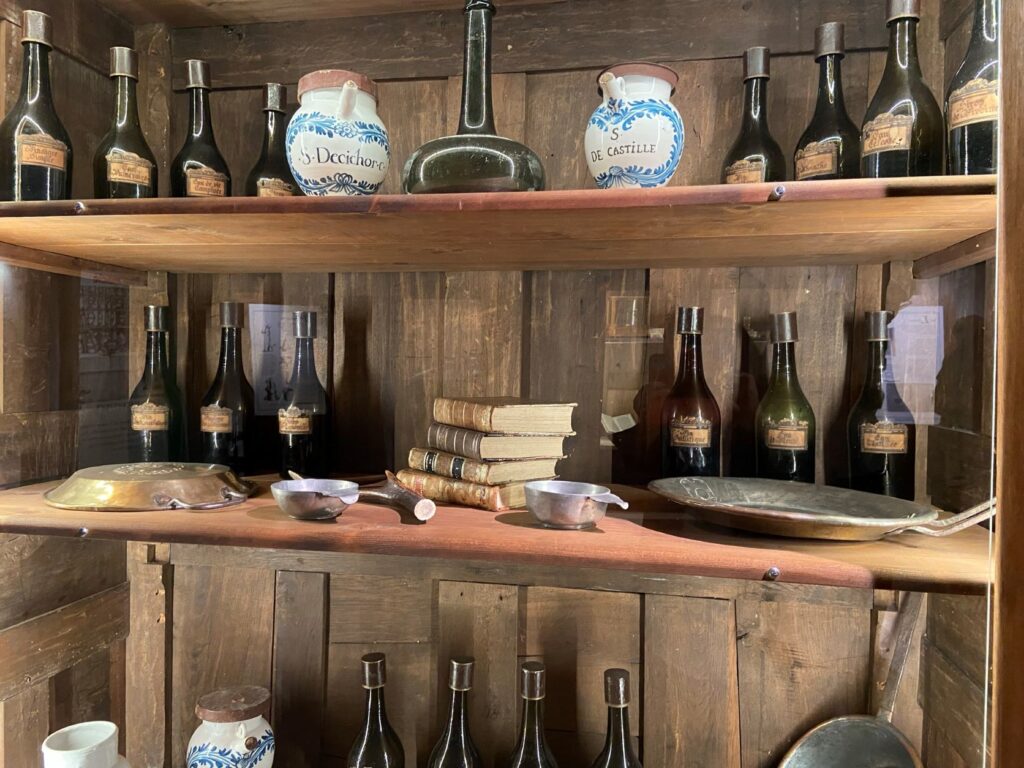 Estantes en un antiguo armario de madera que muestra botellas y frascos antiguos, así como libros de medicina en la botica de Bauge