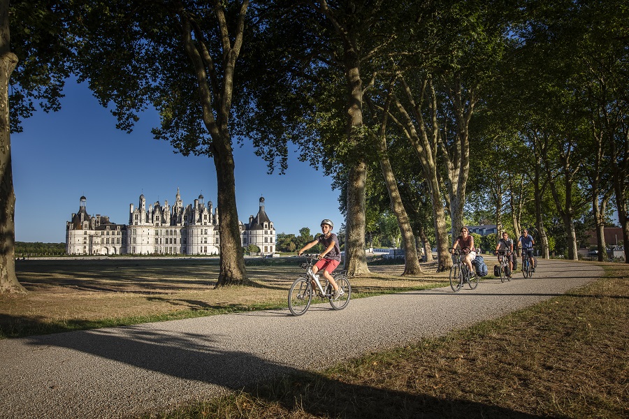 Chambord Chateau, piedras blancas en el fondo del parque y ciclistas en el camino de enfrente