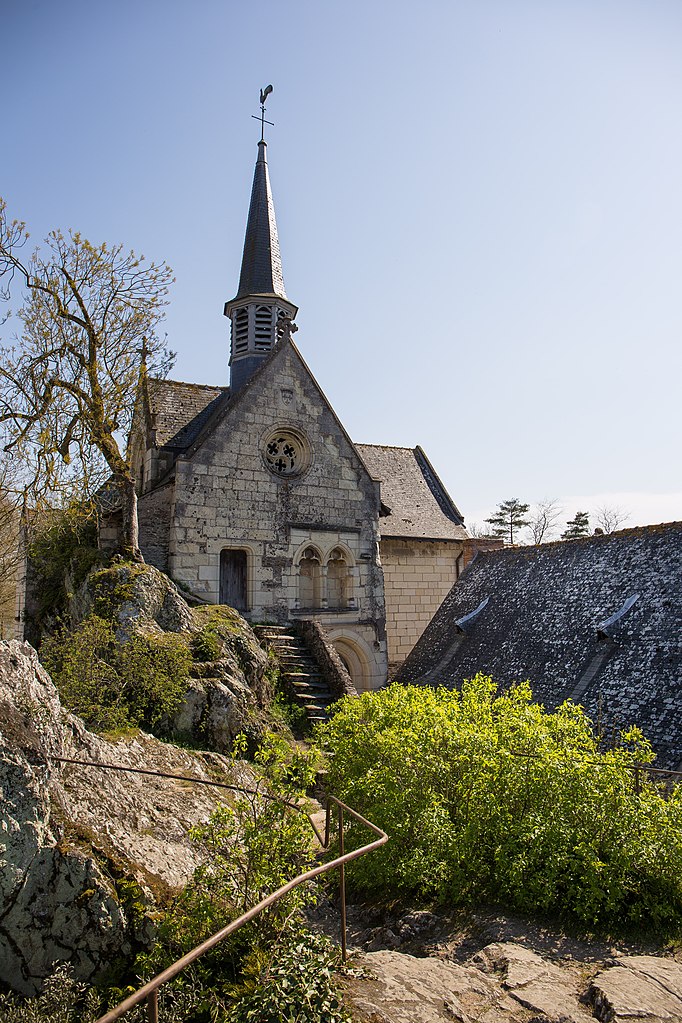 Iglesia Beuard desde el lado y un jardín verde. Una pequeña iglesia muy antigua del siglo XVI con un ábside y una pequeña aguja.