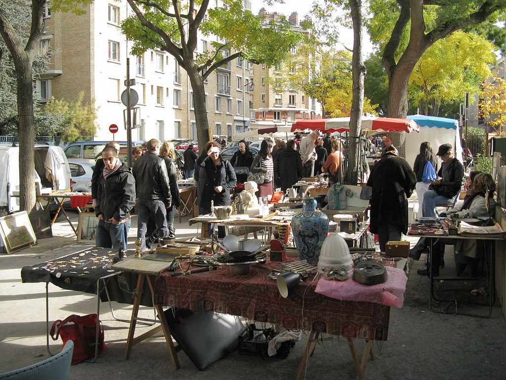 Mercado de pulgas Puces de Vanves en París con gente de la calle pasando por mesas instaladas en la acera llenas de artículos extraños, desde máscaras africanas hasta insignias