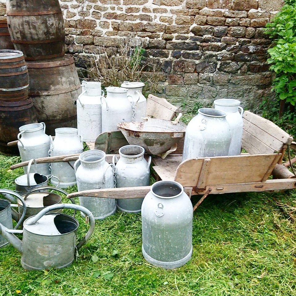 Antiguo granero de sidra en Normandía con muchas jarras de leche de metal en el suelo y una vieja carretilla de madera