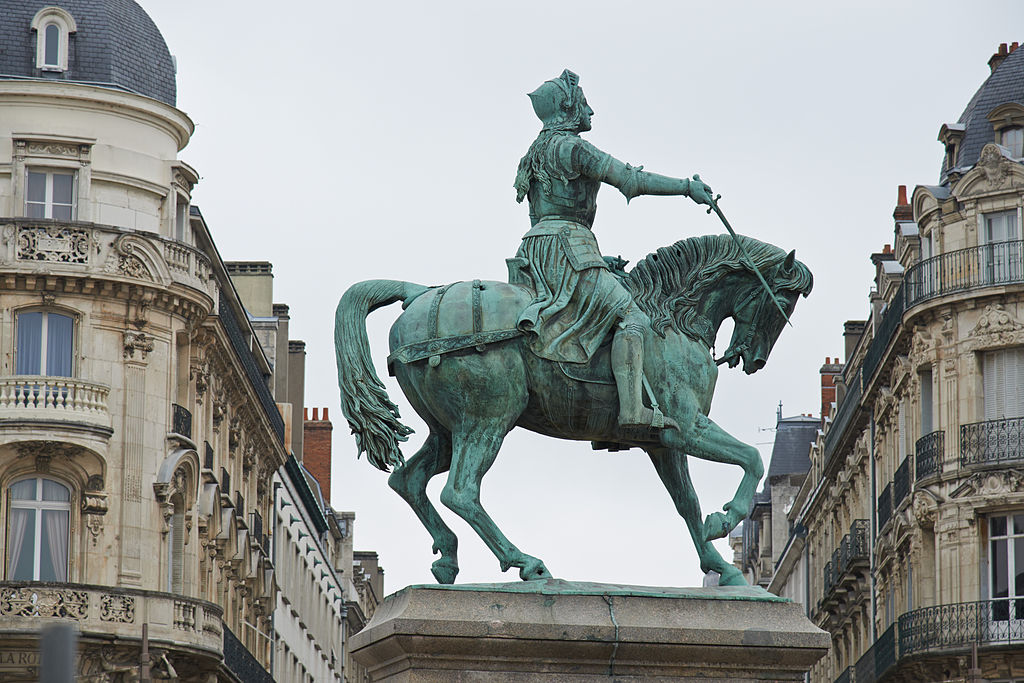 Una estatua de bronce verde de Juana de Arco mirándola sobre un caballo en la plaza principal de Orleand