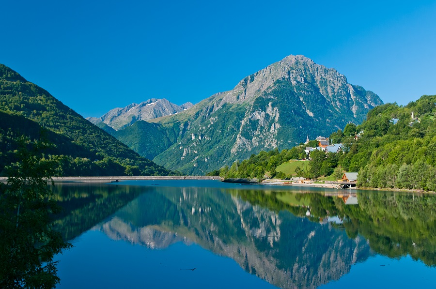 Montañas Oisans en Isère una vista larga sobre un lago con una montaña detrás visible en aguas azules y colinas más pequeñas a ambos lados de una pequeña ciudad