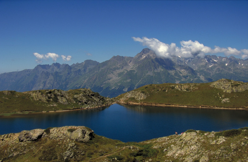 Un lago de montaña azul oscuro en Oisíní con una costa verde al frente y un lago y montañas circundantes al fondo