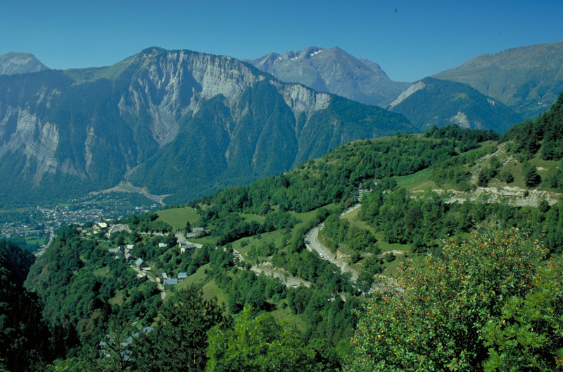 Un plano general de la estrecha carretera que sube por el valle hasta Alpe d'Huez con una montaña al fondo