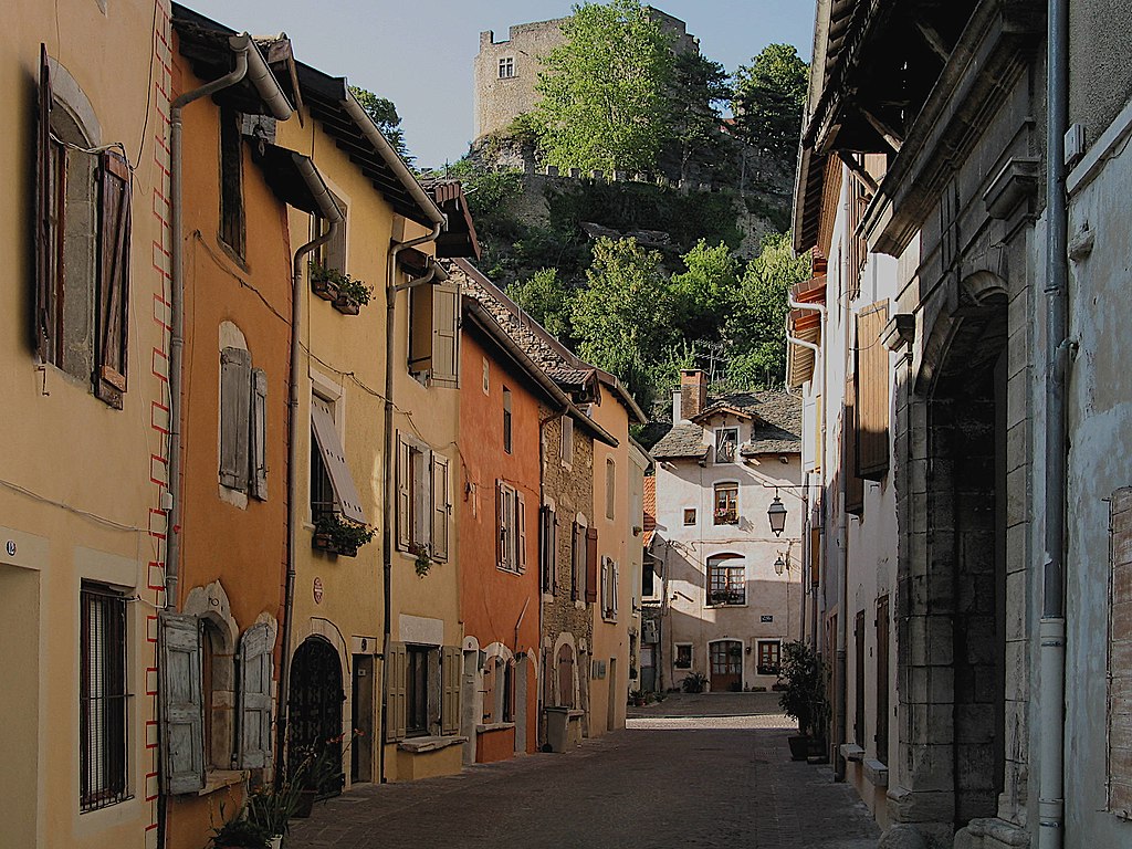 El pueblo medieval de Crémieu con vistas a las estrechas calles flanqueadas por casas de color naranja, rojo y ocre con una montaña al fondo