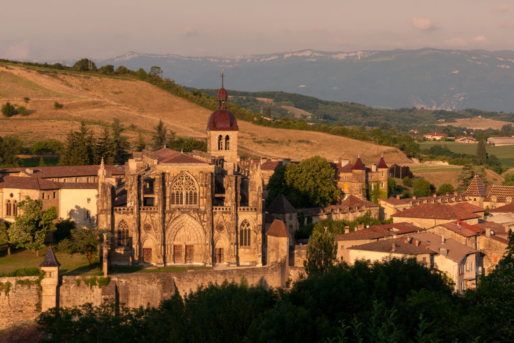 Saint-Antoine de l;Abbaye mirando desde la distancia a la gran catedral completa a la luz del sol naranja y colinas y montañas detrás