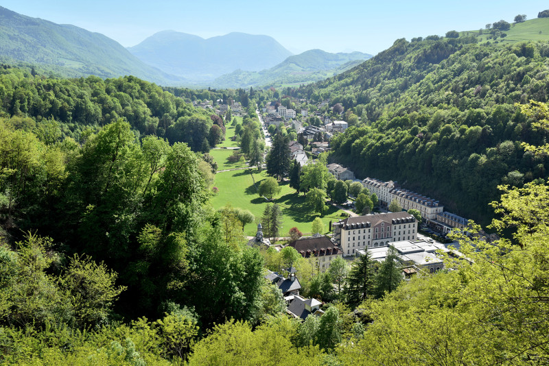 Mirando hacia abajo desde lo alto sobre un valle con montañas al fondo y los edificios de Uriage-les-Bains Spa