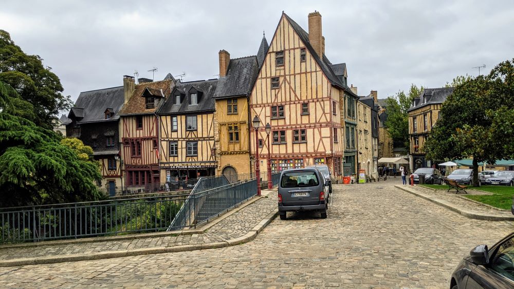 Vista medieval de Le Mans desde un lado de la plaza que muestra un edificio con entramado de madera en la esquina de una oficina de turismo y parte de una hilera de casas similares