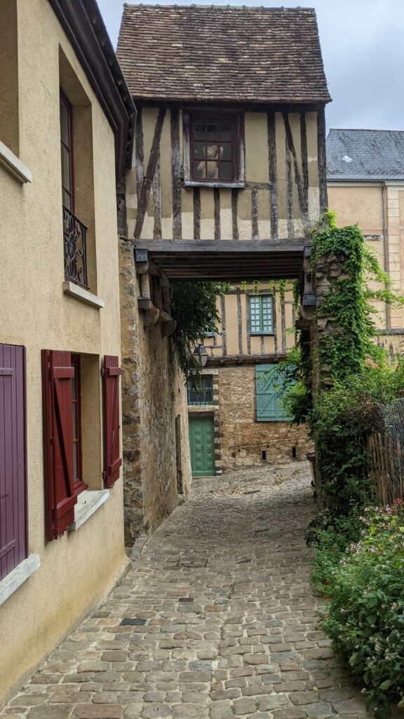 Una casa a la izquierda y un pasaje debajo de una casa con entramado de madera colgada en Le Mans medieval