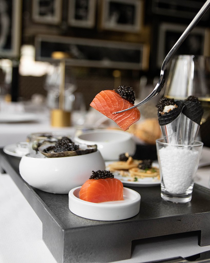 Un plato en el Café Prunier Paris. Salmón rosado cubierto con carriar en la punta del tenedor con otros platos blancos de caviar al lado de la elegante mesa negra