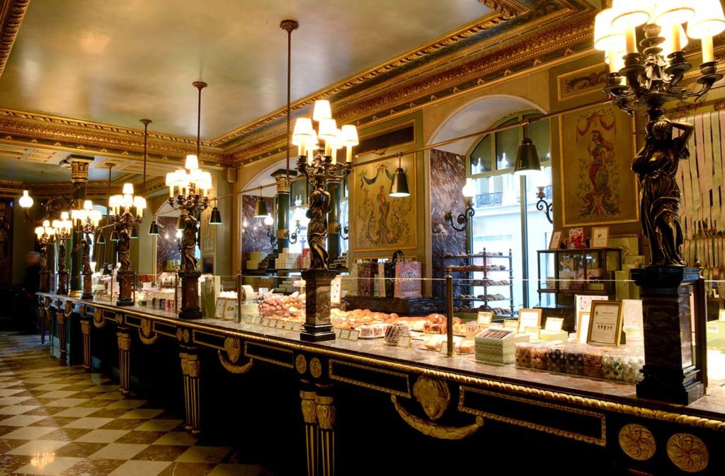 Dentro de Ladurée en París haciendo decoraciones Art Deco con enormes lámparas antiguas, ventanas y un mostrador con alimentos