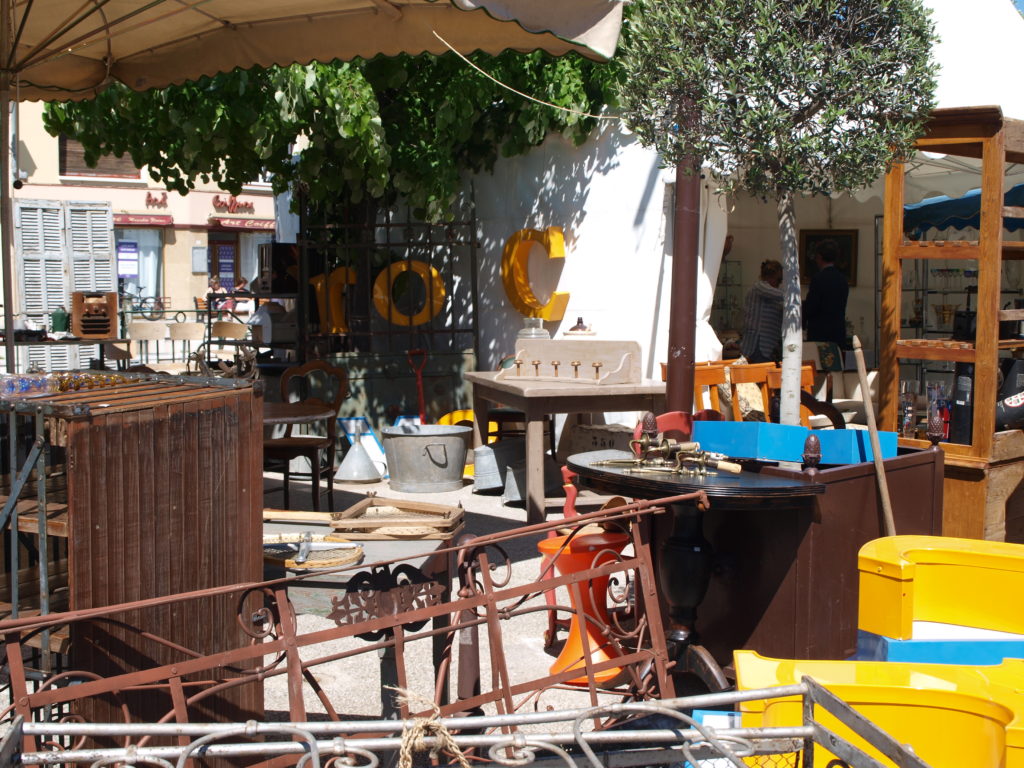 Feria de antigüedades de L'Isle-sur-la-Sorgue con mesas llenas de todo tipo de antigüedades extrañas en una calle arbolada