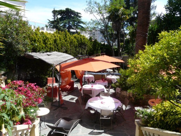 Jardín del Hotel Alexandra con sombrillas naranjas sobre mesas y vegetación y flores.