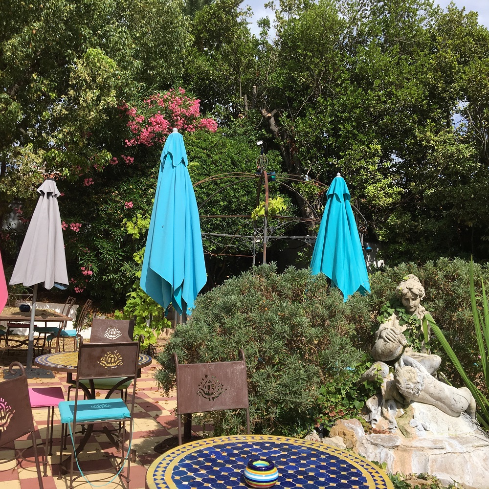 Jardín del hotel Le Pre Catalan con sombrillas, estatuas, pequeña fuente y árboles