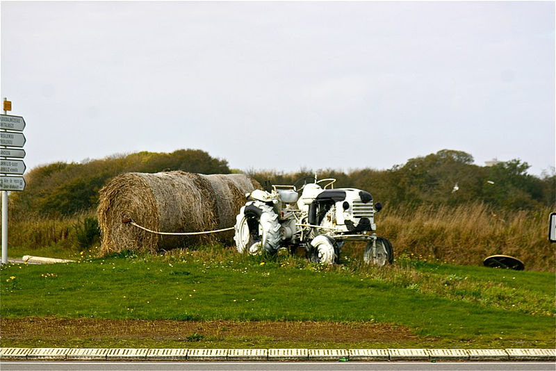 Un tractor blanco y negro con hierba seca detrás en una rotonda en Francia