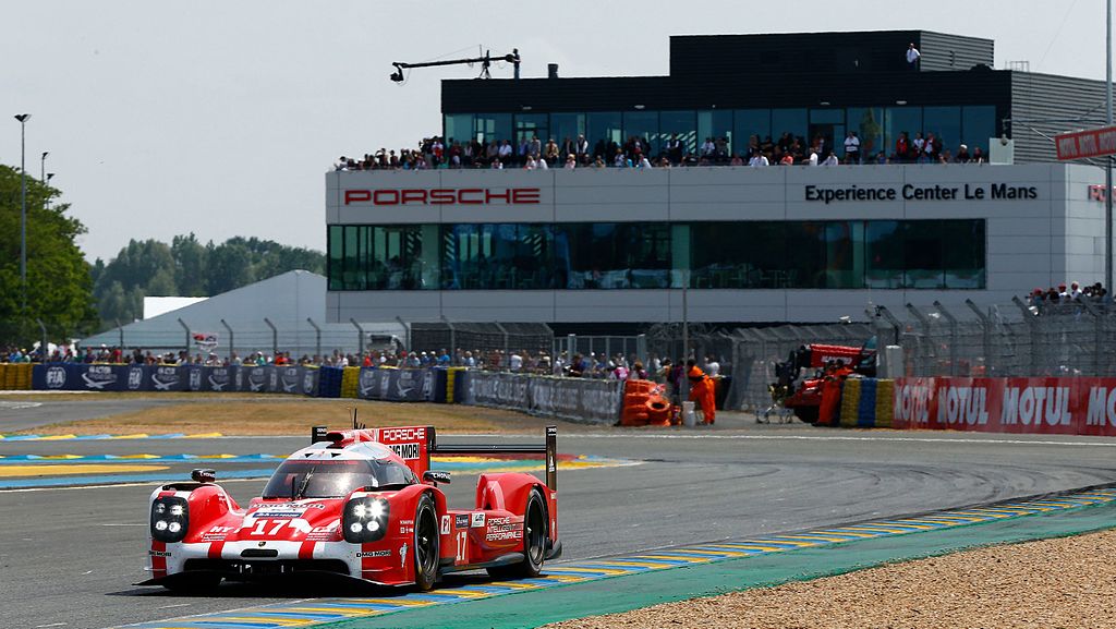 El Porsche Experience Centre de Le Mans con un gran edificio industrial de 3 plantas detrás, gente detrás de las vallas y un Porsche rojo delante