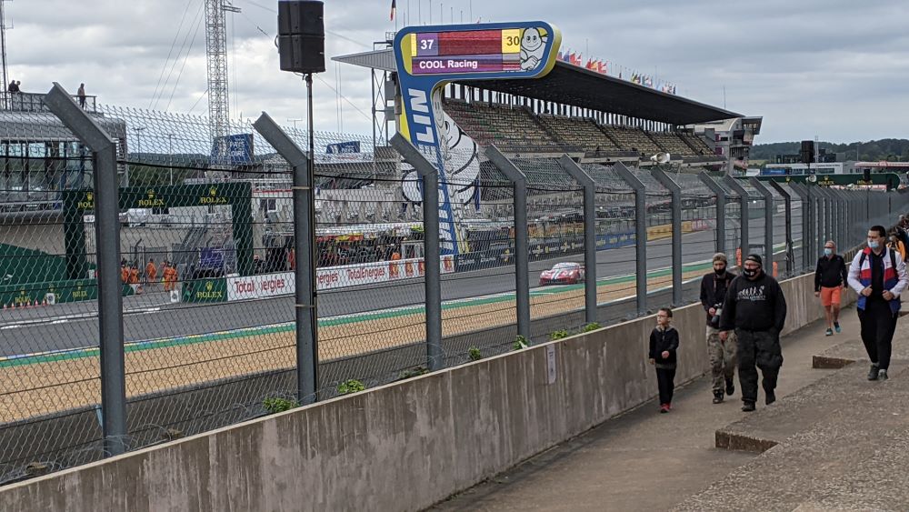 Mirando a través de una barrera de metal en la pista de carreras de Le Mans con gradas al otro lado