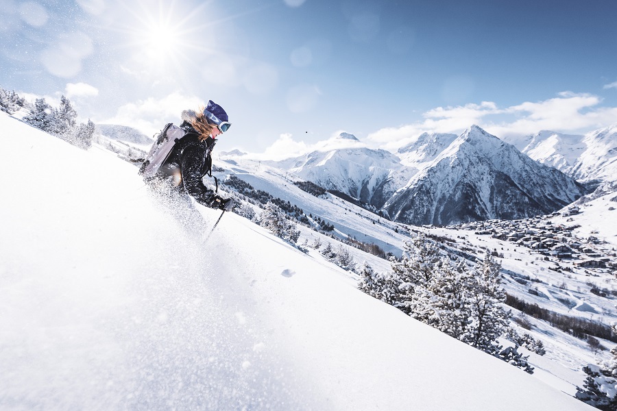 Una mujer a la izquierda esquía rápido en un ventisquero por una pendiente cubierta de nieve en Les Deux Alpes