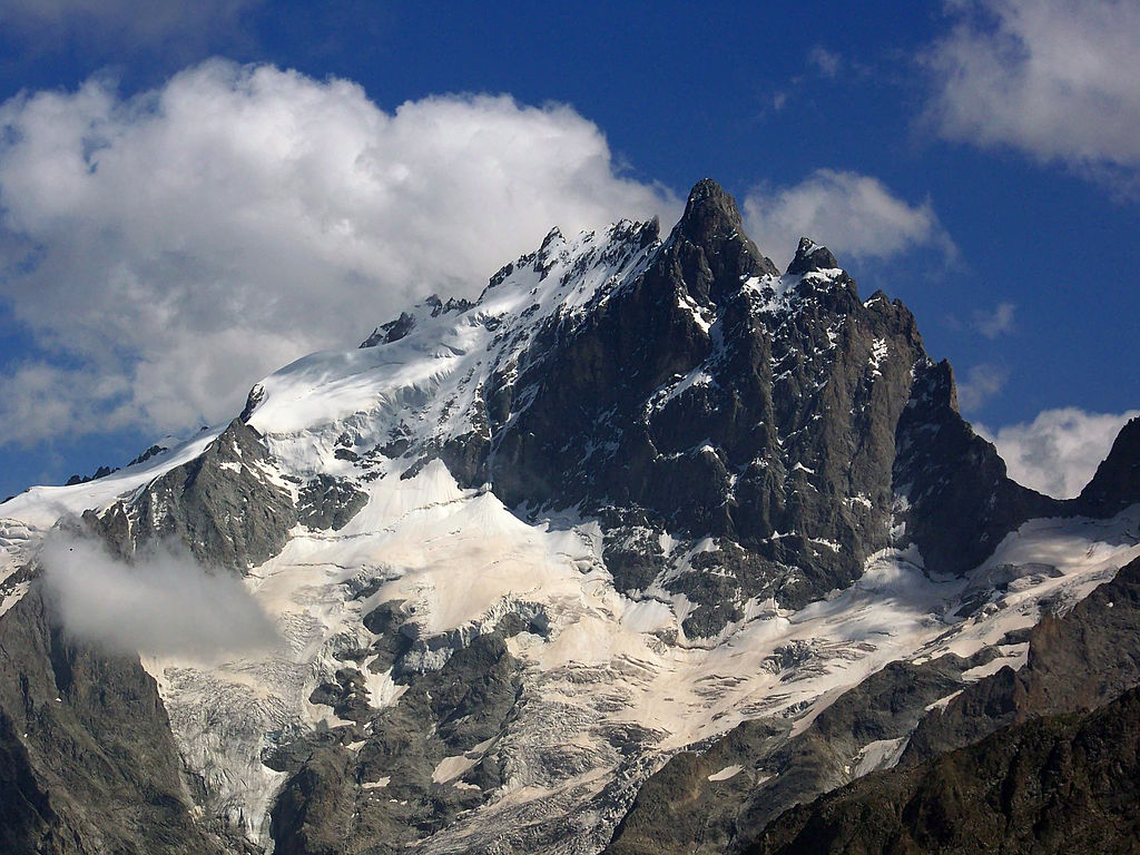 Pic de la Meije en Ecrins mostrando un pico alto hacia arriba de roca parcialmente nevada y laderas nevadas inferiores contra un cielo azul con scat