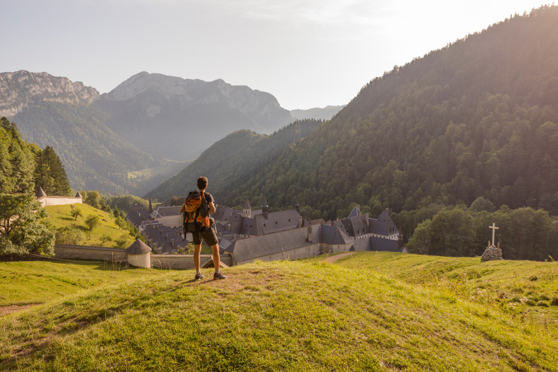 Un paseo por el parque nacional regional de Chartreuse con una persona parada en el parque mirando hacia el monasterio de La Grand Chartreuse y las montañas nubladas detrás