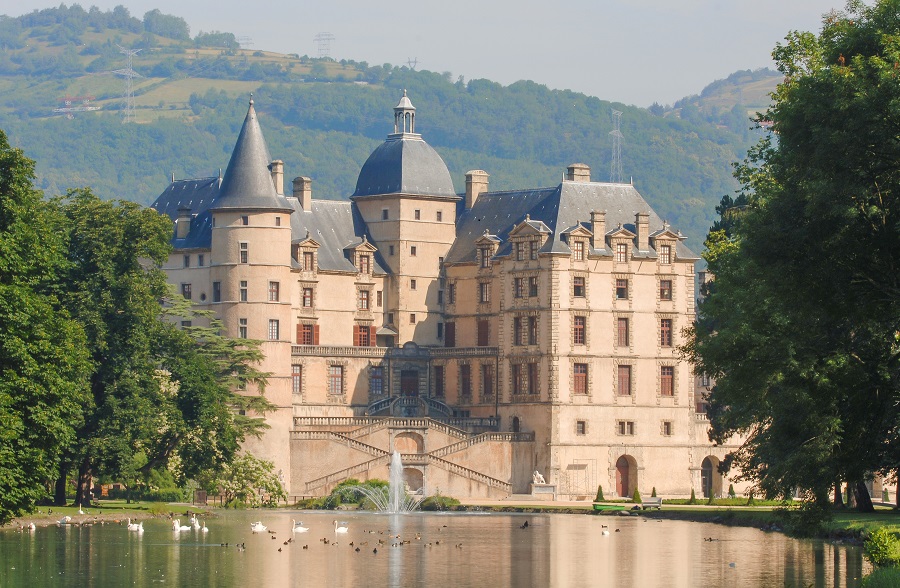 El castillo de Vizille alberga el museo de la resistencia francesa con un lago al frente y un cálido castillo de piedra roja de 5 pisos con techo abuhardillado y montañas detrás