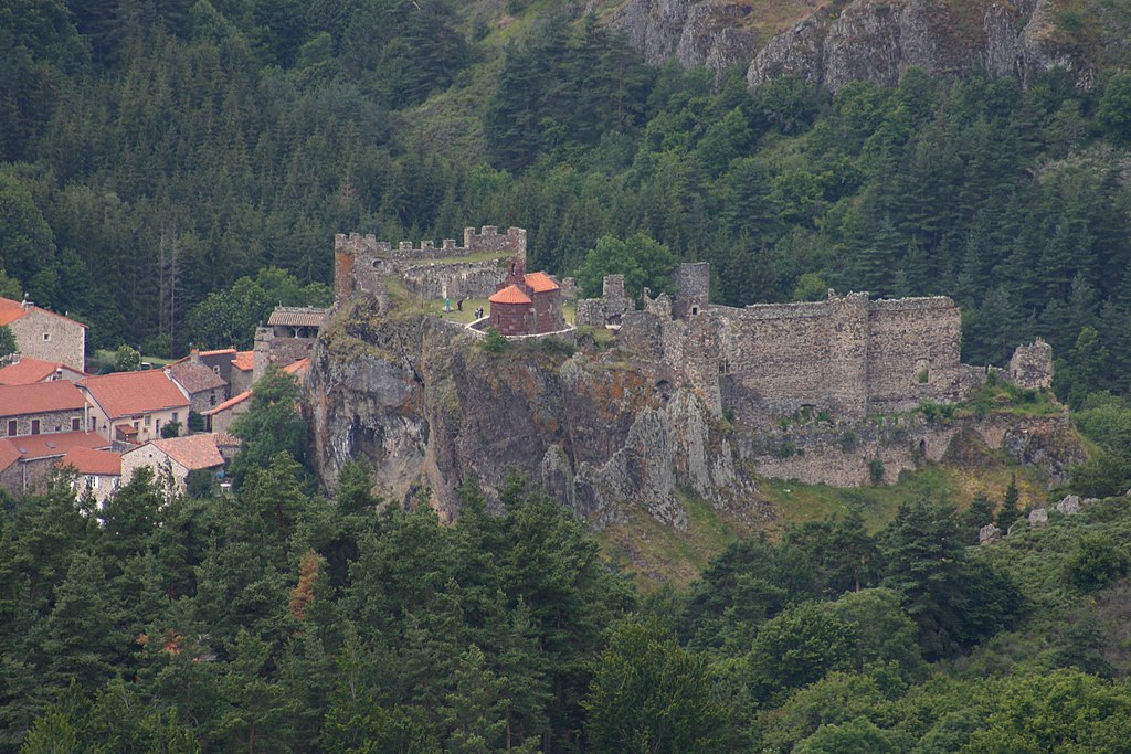 Pueblo de Arlempdes desde arriba que muestra el castillo en ruinas en una colina sobre el pequeño pueblo de casas de piedra y techos rojos