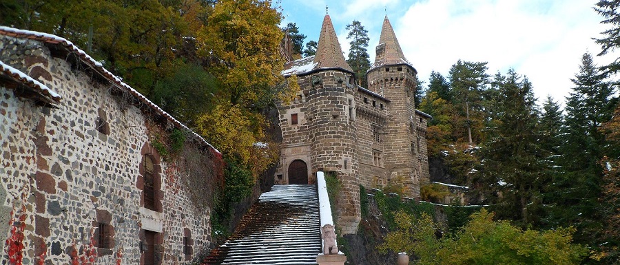 Chateau de la Rochelambert mirando hacia un camino empinado hacia la puerta principal con un pequeño castillo con torretas contra la colina