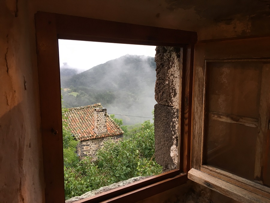 mirando a través de una pequeña ventana de madera en una casa amurallada de piedra con techo rojo y niebla en aumento