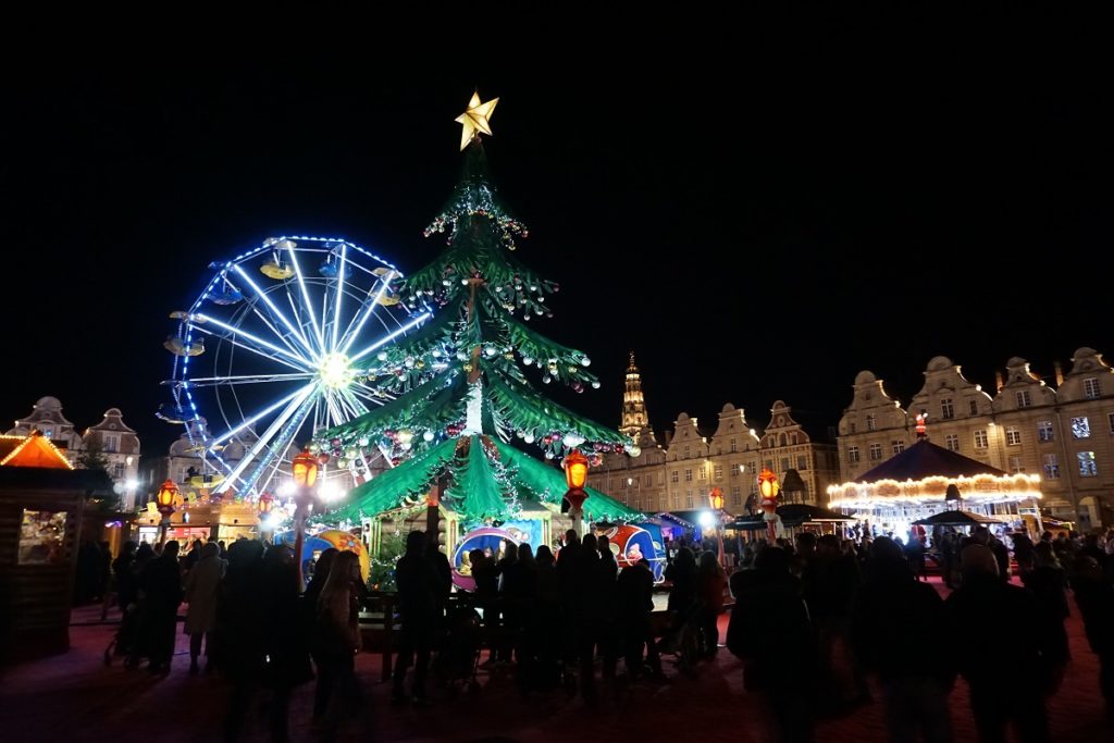 Mercado de Navidad de Arras por la noche con una gran rueda azul iluminada, un gran árbol de Navidad y gente en la plaza principal