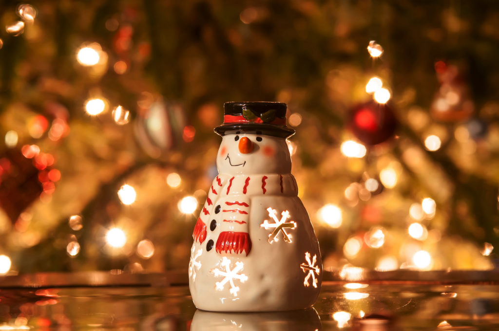 Vela navideña muñeco de nieve con cara, sombrero, bufanda contra el fondo de las luces