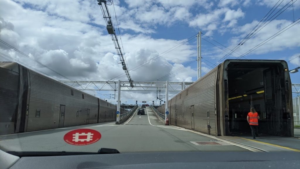 Eurotunnel en Calais con trenes a ambos lados y la carretera en el medio y un automóvil en la parte superior de la pendiente por delante