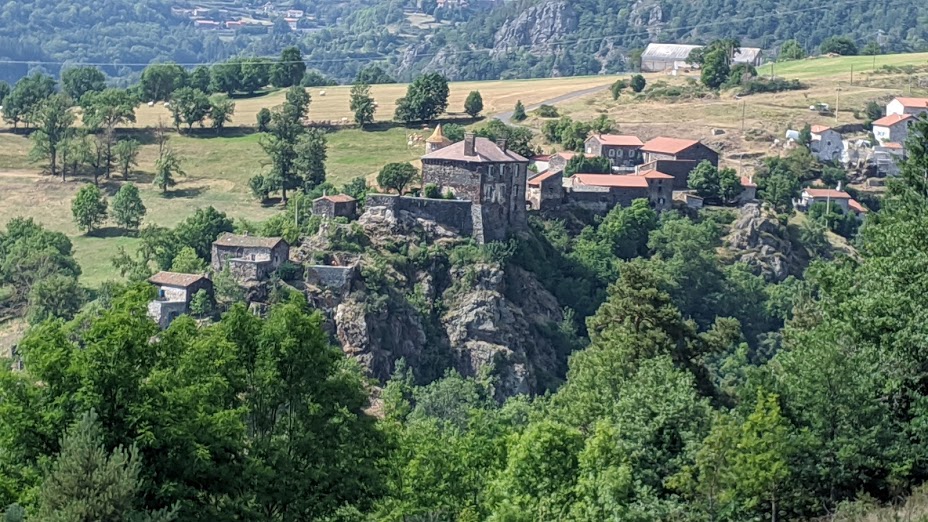 Una vista desde arriba de un pueblo de Auvernia encaramado en una ladera rocosa. Antiguo castillo y casas de piedra con techos de tejas rojas