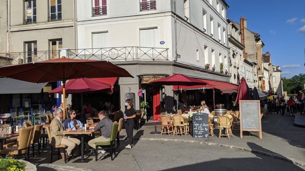 Bistrot en vista exterior de Fontainebleau con mesas en la terraza, talbes, sillas, comida para personas y alitas rojas