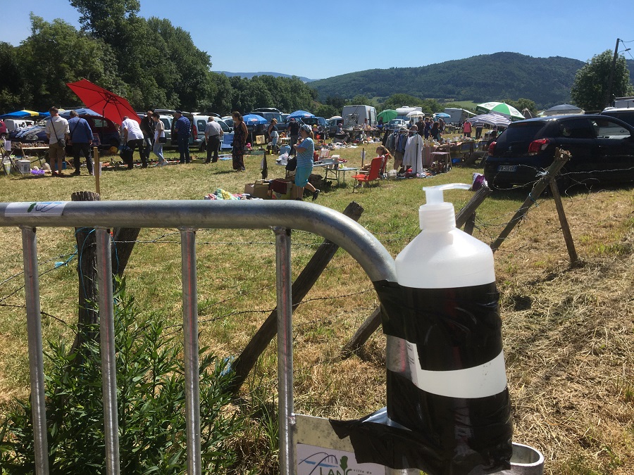 Botella sanitaria de plástico pegada a una valla metálica con puestos detrás en el campo en grenier vide