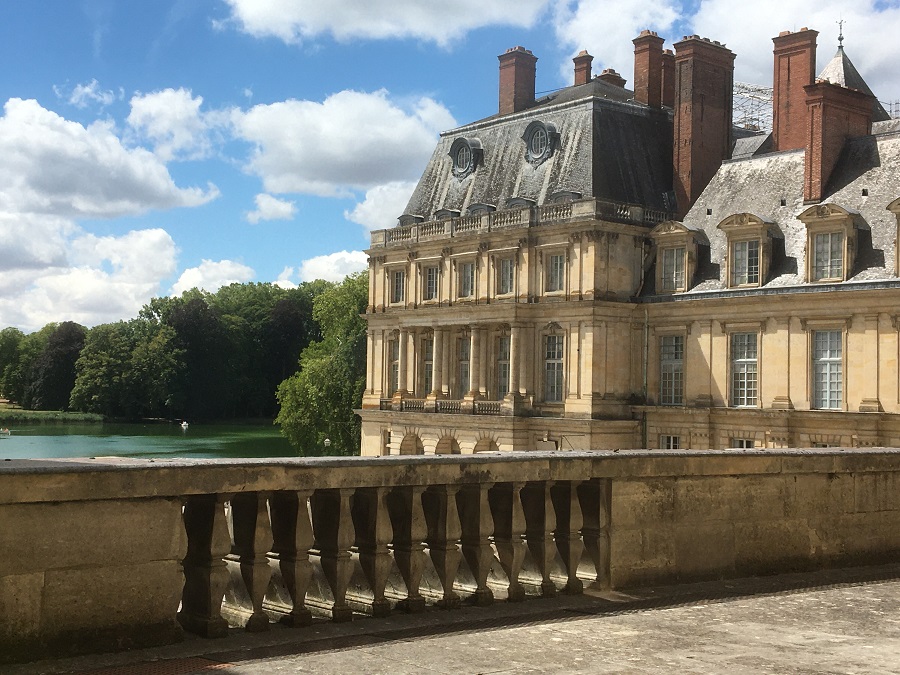 Un ala de Fontainebleau con terraza delantera y balaustrada de piedra, y un edificio de piedra cálida de 3 pisos con ventanas abuhardilladas y techo a dos aguas detrás