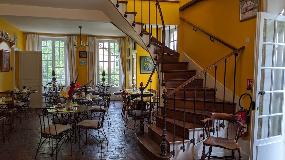 Desayuno en el Hotel Les Grands Chenes en una bonita sala amarilla con mesas puestas y una escalera de caracol en el frente