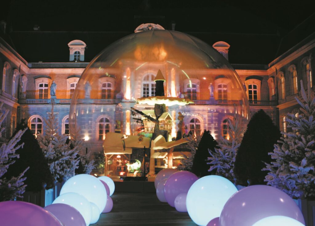 Mercado navideño de Amiens que muestra grandes luces circulares alternas de color púrpura y blanco que conducen a una burbuja transparente gigante fuera del ayuntamiento iluminado