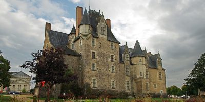 Chateau de Bauge en Glenloir con un cielo tormentoso y un enorme castillo con torres y techos cónicos y jardines en frente