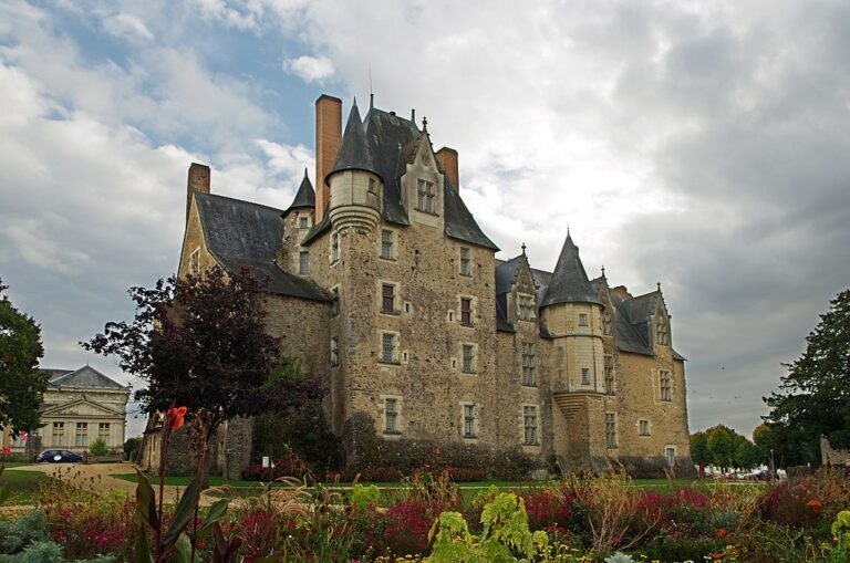 Chateau de Bauge en Glenloir con un cielo tormentoso y un enorme castillo con torres y techos cónicos y jardines en frente