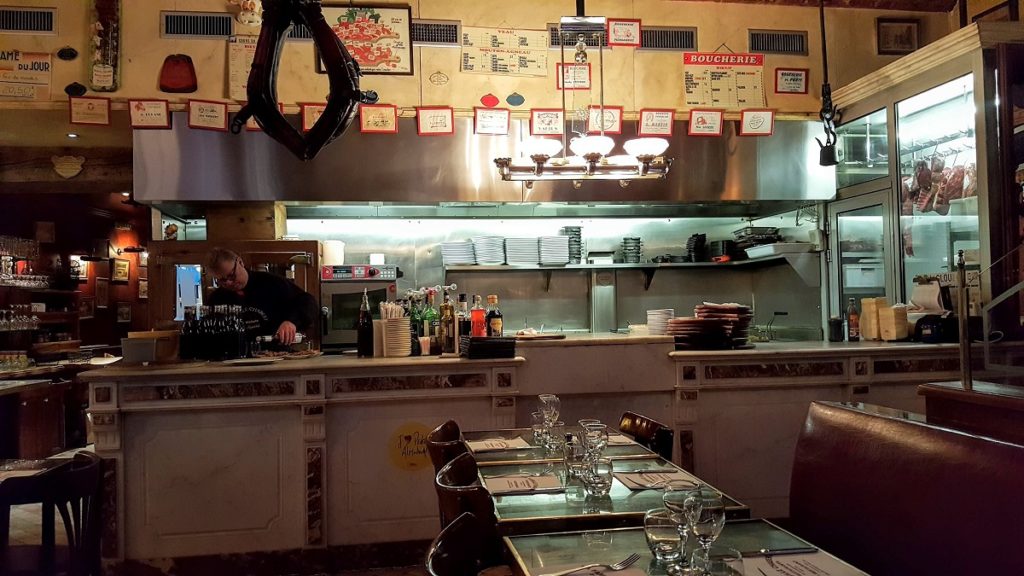 Restaurante Bouchon en Lyon con un mostrador de carne, avisos en las paredes y mesas en el frente