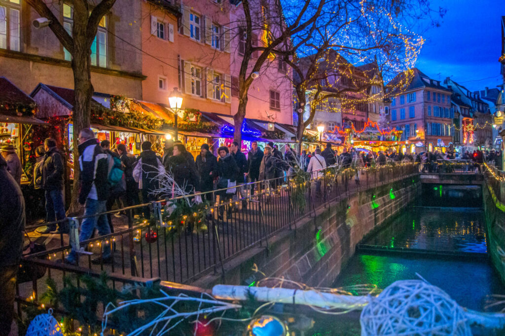 Mercado navideño de Colmar junto al río con el río a la derecha y puestos en la orilla iluminados con casas antiguas detrás