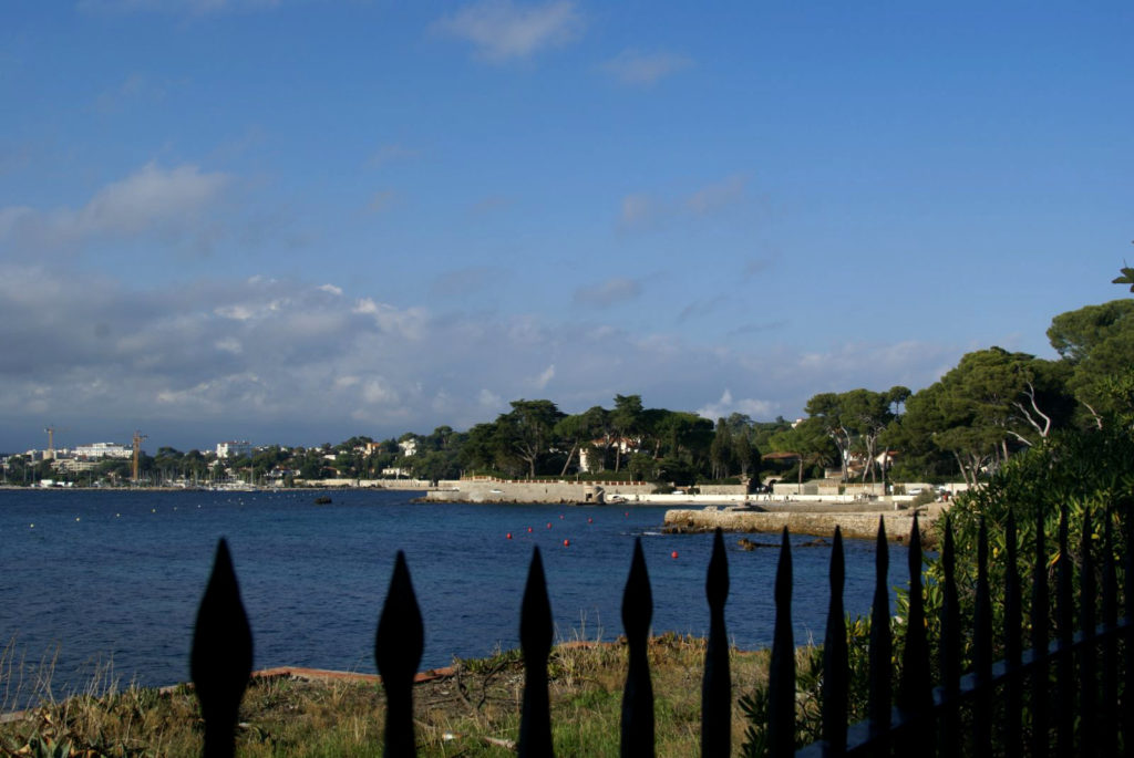 Vista de Juan les Pins desde la carretera con árboles, mar y edificios al fondo