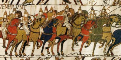 Tapiz de Bayeux con muchos soldados ingleses a caballo en colores cálidos con bestias en el panel inferior y pájaros y dos hombres luchando en el superior