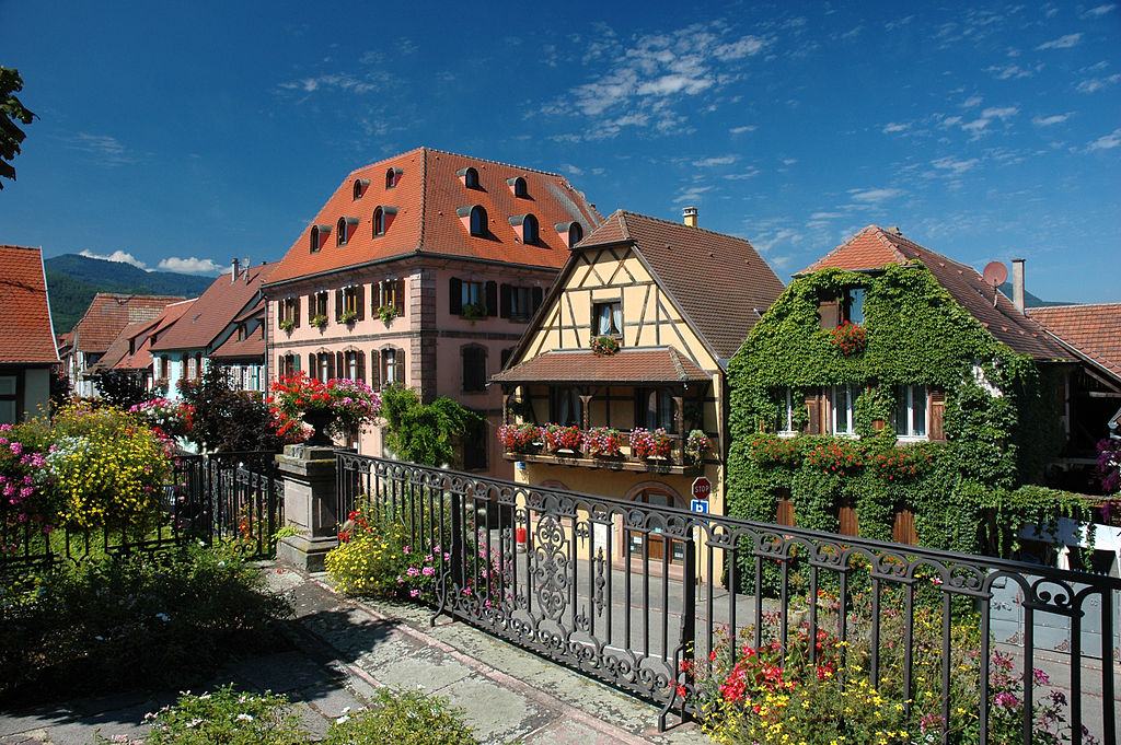 Aldea de Bergheim Alsacia con una vista oblicua de grandes casas con techos inclinados en la calle con árboles verdes